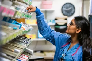 Aditi, Patel, Pharmacy Manager at Tufts Medical Center, reaches for a bottle of medication in supply room.